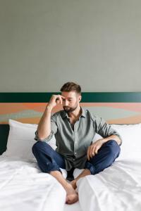 un hombre sentado en una cama hablando por celular en Stadthotel Freilassing, en Freilassing