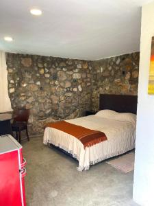 1 dormitorio con cama y pared de piedra en Cabaña El Fantasio en Villa Carlos Paz