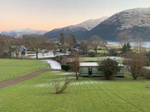 a green building in a field with mountains in the background at Sandpiper Caravan in Onich