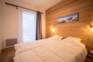 a bedroom with a white bed with a wooden wall at Résidence LUMI BATIMENT B - Appartement LUMI B 814 in Valmorel