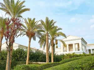 a white house with palm trees in front of it at Grecotel La Riviera & Aqua Park in Loutra Killinis