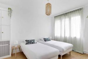 2 camas en un dormitorio blanco con lámpara de araña en Superbe appartement lumineux et calme en Saint-Ouen