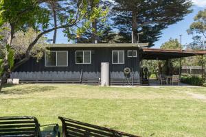 una piccola casa nera con una panchina da picnic in un cortile di Shoreline Sanctuary - A Retro Family Beach Shack a Somers
