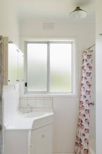 uma casa de banho branca com um lavatório e uma janela em Shoreline Sanctuary - A Retro Family Beach Shack em Somers