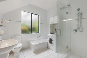 Waiheke Island Resort Conference & Accomodation Centre في Ostend: حمام ابيض مع حوض استحمام وغسالة ملابس