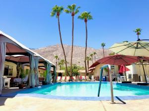 a swimming pool with palm trees and an umbrella at EDR Hotel - Adults Only & Clothing Optional in Palm Springs