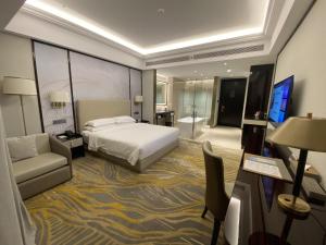 una camera d'albergo con letto, divano e TV di Grand New Century Hotel Binjiang Hangzhou a Hangzhou