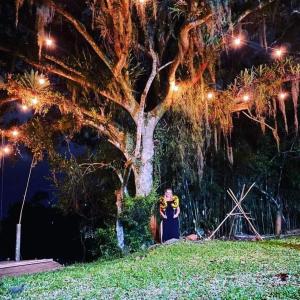 Sítio com piscina Hidromassagem com acesso ao Rio Mampituba في باسو دي توريس: امرأة تقف أمام شجرة في الليل