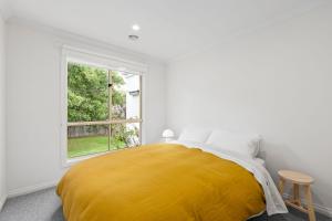 een witte slaapkamer met een geel bed en een raam bij Paddys in Point Lonsdale