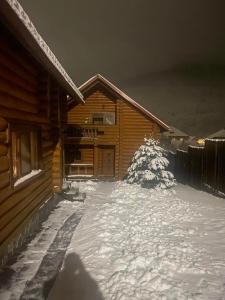 une cabane en rondins avec de la neige devant elle dans l'établissement Smerekovyi Dvir, à Polyana