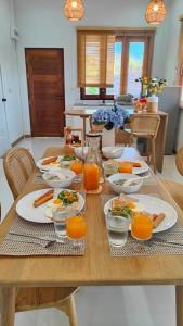 a wooden table with plates of food and orange juice at บ้านข้าวหอม บึงโขงหลง in Ban Sok Pho