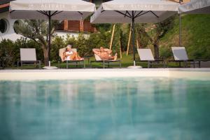 una piscina con 2 personas sentadas en sillas y sombrillas en Glamping Alvearium Alturis en Gagliano