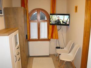 a living room with a tv and chairs and a window at Ezüsthíd Apartman in Balatongyörök