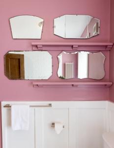 a bathroom with three mirrors on a pink wall at Pebble Cottage in Seahouses