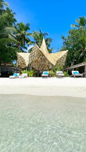 a beach with chairs and a resort with palm trees at Thari Fushi Luxury Maldivian Experience - All Inclusive in Thinadhoo