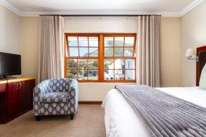 Noordhoek Village Hotel في نوردهوك: غرفة نوم بسرير وكرسي ونافذة