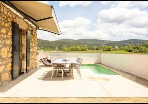 een patio met een tafel en stoelen en een zwembad bij La Grange de Papy in Vallon-Pont-dʼArc