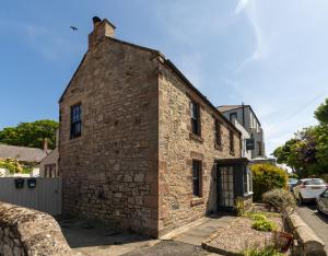 an old brick building with a door on a street at Rose Cottage by Coast & Country Stays in Beadnell