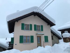 dom pokryty śniegiem z zielonymi okiennicami w obiekcie Chalet del Sole w mieście Quinto