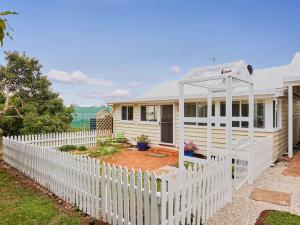a white picket fence in front of a white house at Moonya Avocado Farm Cottage - with early check-in in Mount Tamborine