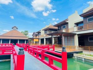 uma ponte vermelha sobre a água em frente a alguns edifícios em COZY SHIROI RESORT em Nang Rong