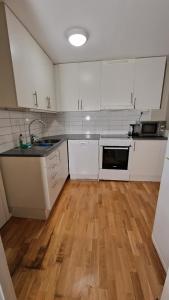 a kitchen with white cabinets and a wooden floor at Mysigt Stadsoas: En Modern lägenhet med 2 sovrum in Gothenburg