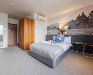 una mujer sentada en una cama en una habitación de hotel en Hotel Relief Kokura Annex, en Kitakyushu