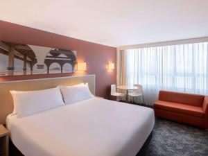 um quarto de hotel com uma cama branca e uma cadeira vermelha em Mercure Newcastle em Newcastle