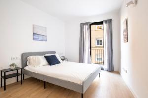 a white bedroom with a bed and a window at Centric Apartment Camp Nou in Hospitalet de Llobregat