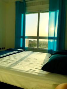 a bedroom with a bed with blue curtains and a window at NOUVEAU, Residence Cap Spartel avec une vue sur mer in Tangier