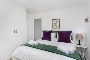 a white bedroom with a large bed with purple pillows at Coral Island 102 in Bloubergstrand