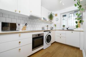 cocina con armarios blancos, lavadora y secadora en Lovely Apartment in Victoria Park Village en Londres