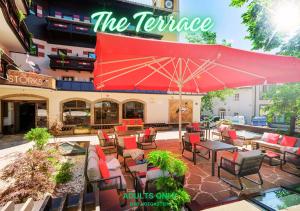 a patio with a red umbrella and tables and chairs at Hotel Bad Hofgastein - The STORKS - Adults Only in Bad Hofgastein