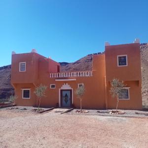 an orange building with trees in front of a mountain at Dar Brahim tizgui nbarda in Ouarzazate
