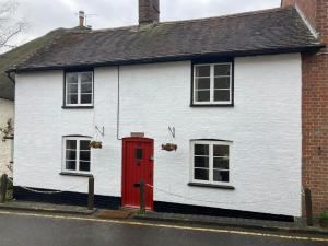 uma casa branca com uma porta vermelha e duas janelas em Nutshell em Sturminster Newton