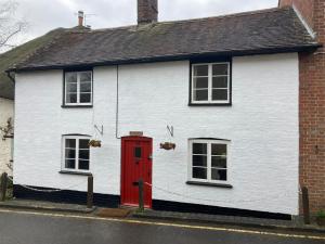 a white house with a red door and two windows at Nutshell in Sturminster Newton