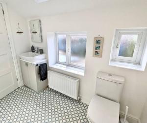 a bathroom with a toilet and a sink and two windows at May Cottage - Boutique Coastal Property. Crabpot Cottages Sheringham in Sheringham