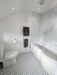 a white bathroom with a toilet and a bath tub at May Cottage - Boutique Coastal Property. Crabpot Cottages Sheringham in Sheringham