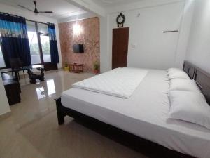1 dormitorio con 1 cama blanca grande y reloj en la pared en Tapovan Farm House, en Sultan Bathery