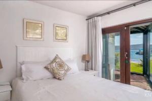 a white bedroom with a bed and a window at Waterfront Apartment in Knysna