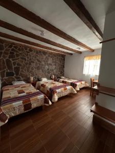 1 dormitorio con 3 camas y pared de piedra en YUMBILLA ECO LODGE, en Cuispes
