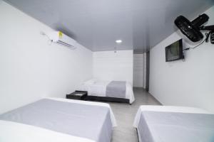 a white bedroom with two beds and a tv at Hotel Santa Marta Tropical in Santa Marta