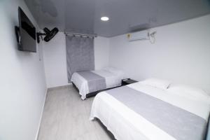 a white bedroom with two beds and a tv at Hotel Santa Marta Tropical in Santa Marta