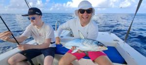 dos hombres sentados en un barco sosteniendo un pez grande en Fish Tobago Guesthouse or Joy and Brandon Guesthouse en Buccoo