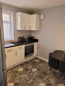 a kitchen with white cabinets and a table and a microwave at Silvertree Lodge - 2 double bed flat with parking in Hemel Hempstead