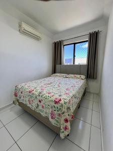 a bedroom with a bed with a floral comforter and a window at Apto próximo à Fac. Pio X in Aracaju