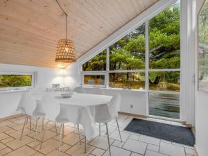 a dining room with a white table and chairs and windows at Holiday Home Emila - 2-2km from the sea in Western Jutland by Interhome in Bolilmark
