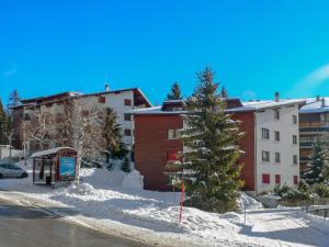 une rue enneigée avec un bâtiment et un arbre dans l'établissement Apartment Violettes-Vacances A-B-C-7 by Interhome, à Crans-Montana