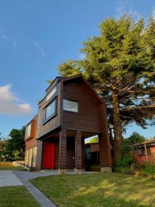 una pequeña casa con una puerta roja y un árbol en AncudLodge en Ancud