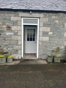 a white door of a brick house with potted plants at Apple Cottage in Newton Stewart